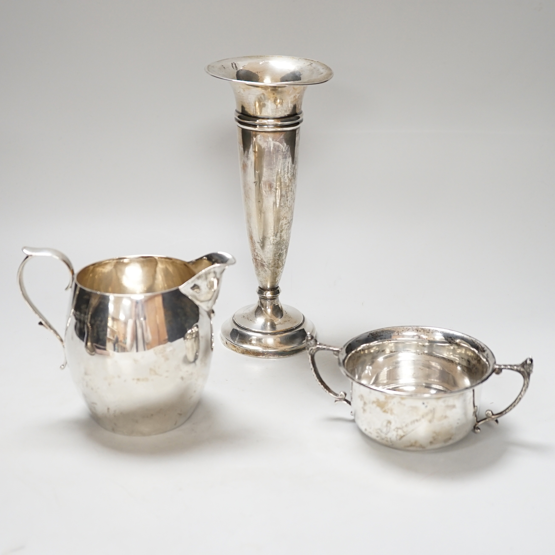 A George V silver cream jug, London 1926, 216 grams, a sugar bowl, Birmingham 1924, 107 grams and a spill vase with loaded base, Birmingham 1919, 20.5cm